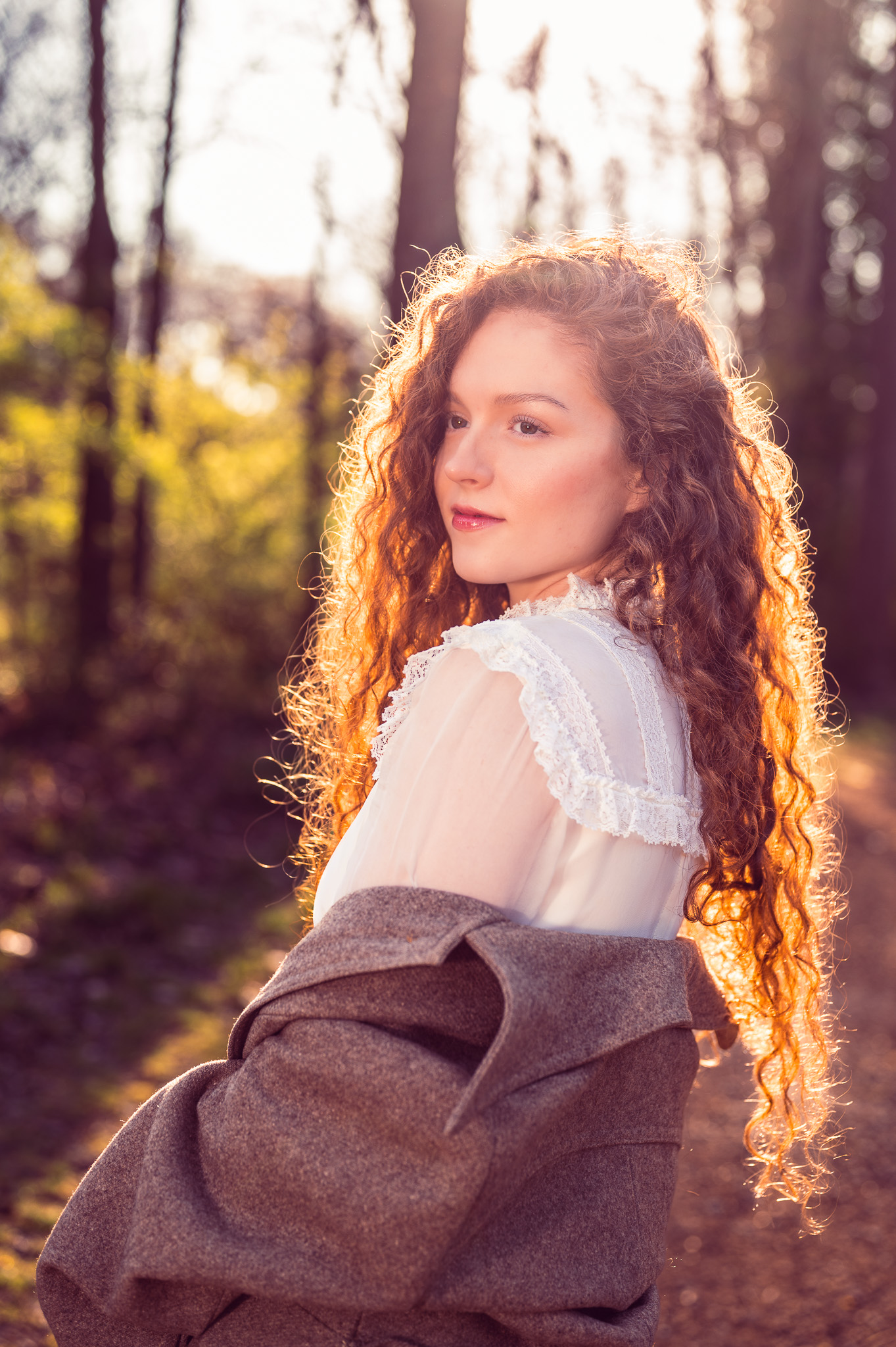 A woman with red hair poses in vintage clothing with backlit by the sun during a morning photoshoot